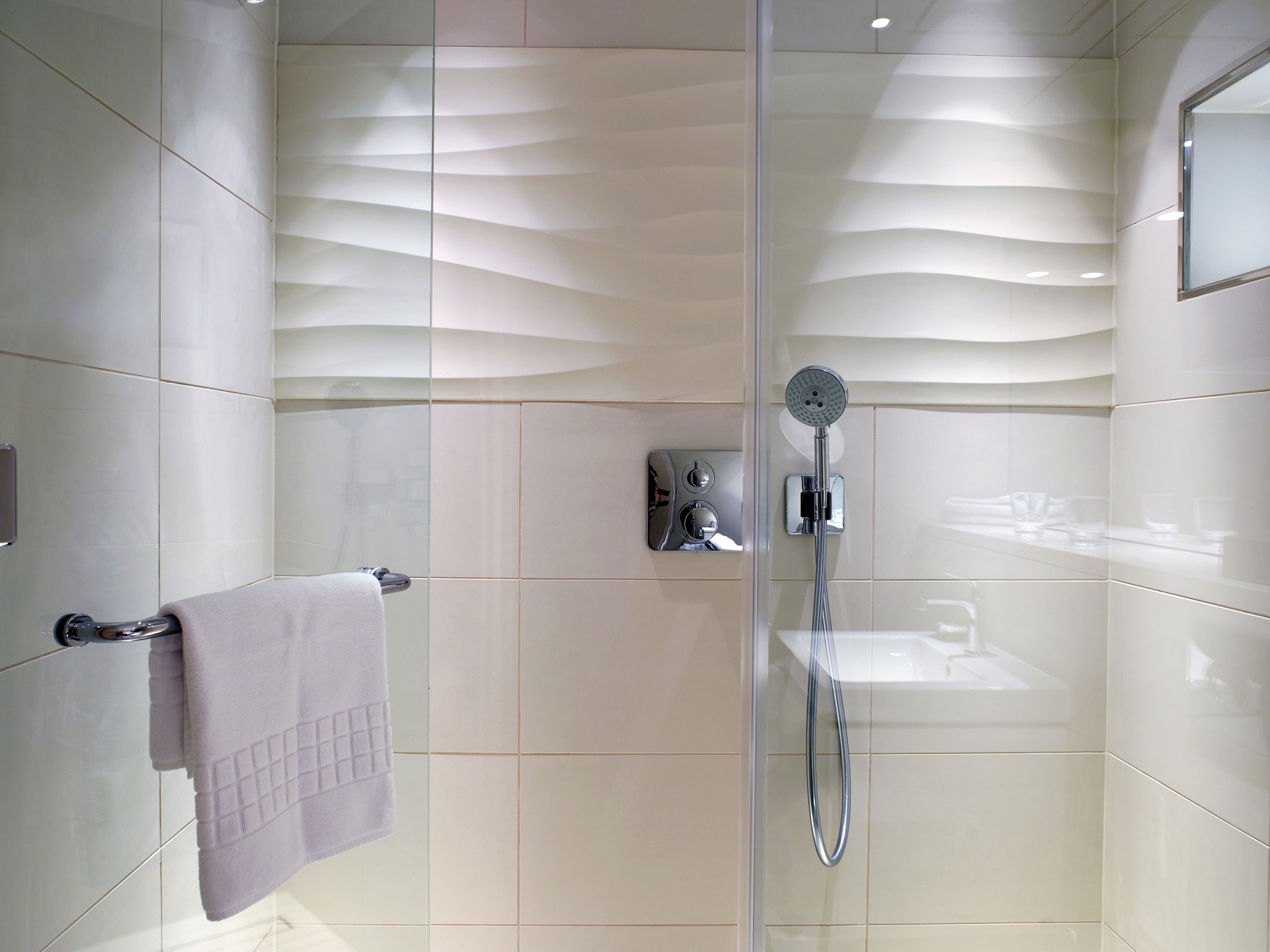Un baño moderno con ducha de vidrio, un perchero con toalla doblada y panel de control en la pared.