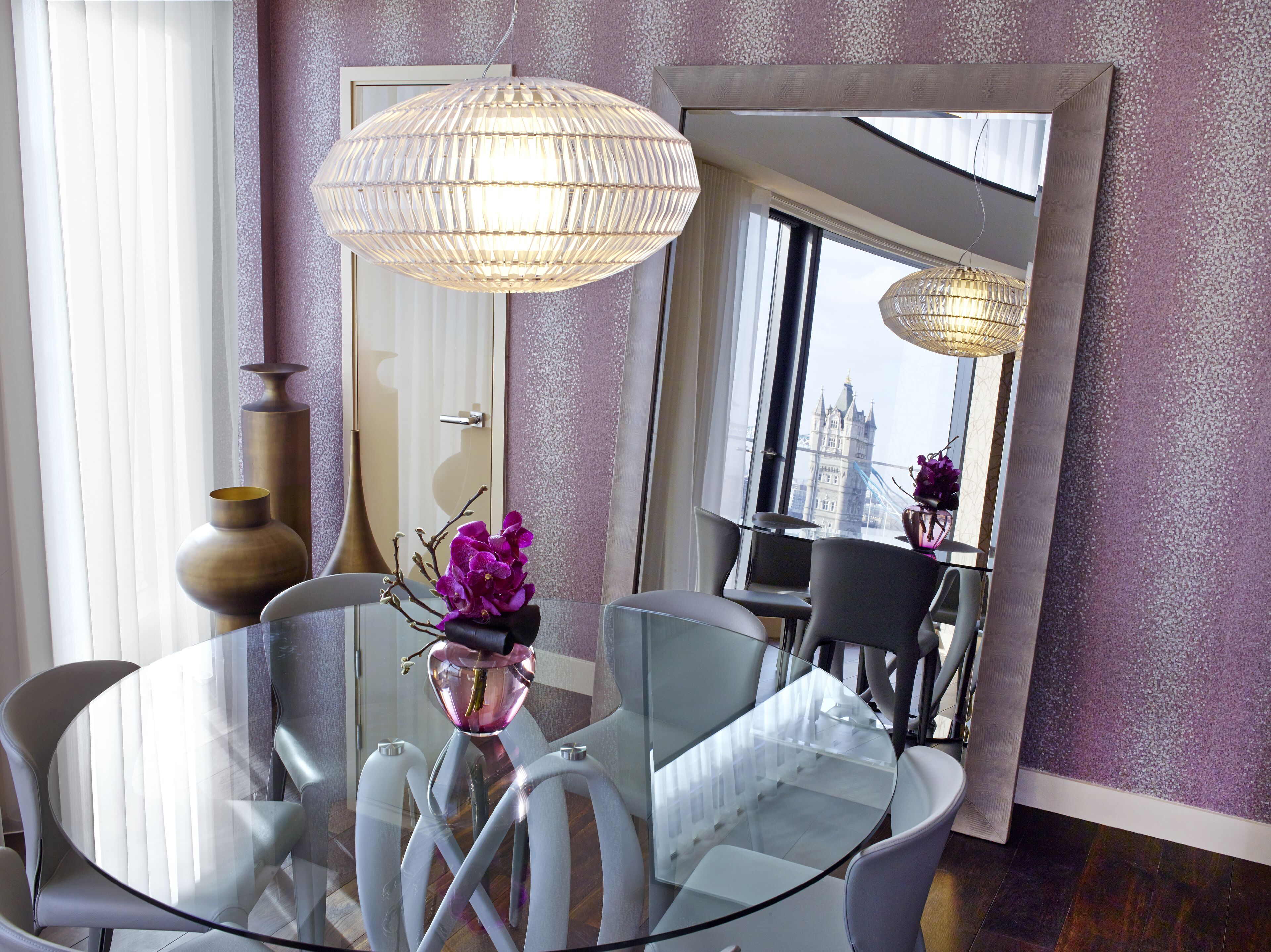Un comedor moderno con una mesa de vidrio, sillas blancas y un jarrón con flores moradas.