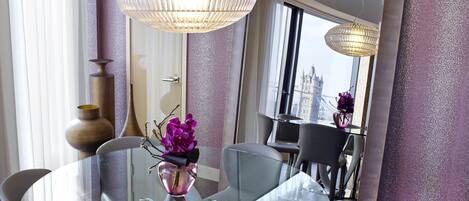 A modern dining area with a glass table, white chairs, and a vase with purple flowers.
