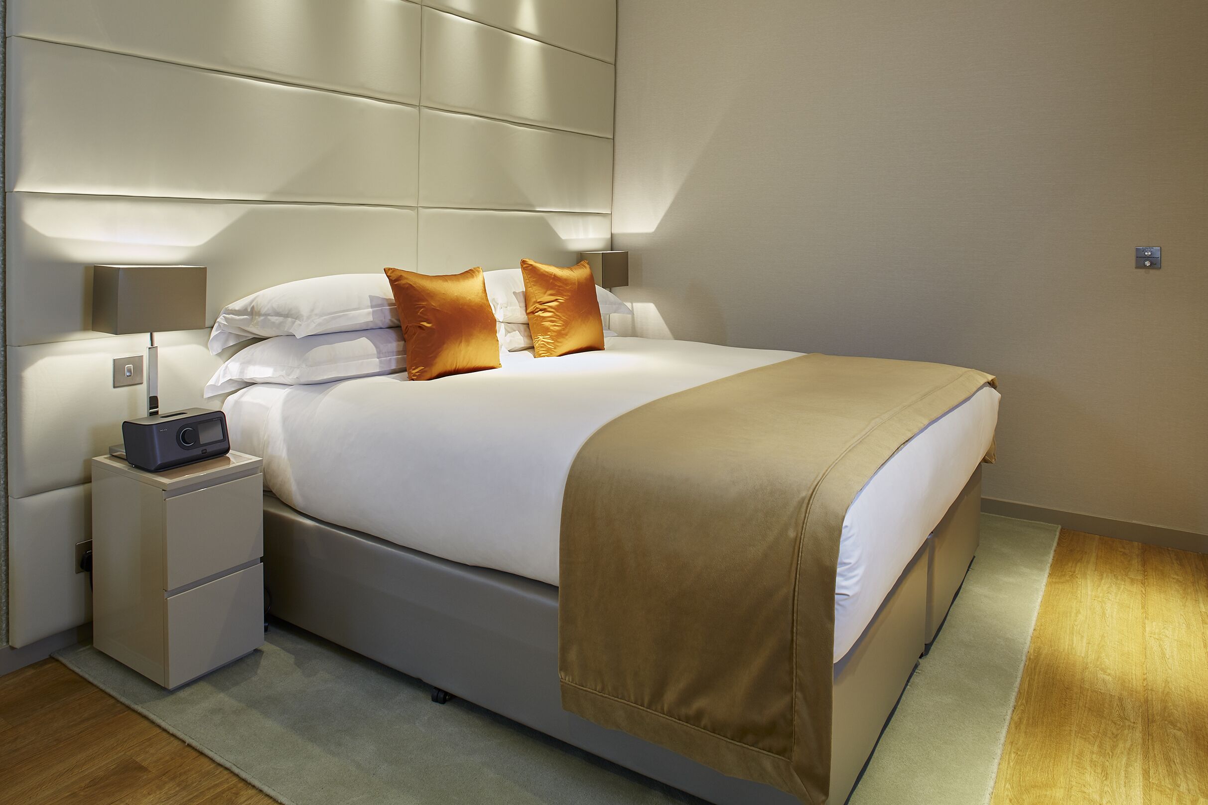 Una habitación de hotel moderna con una cama grande, una mesita de noche con una radio y una lámpara fijada a la pared.
