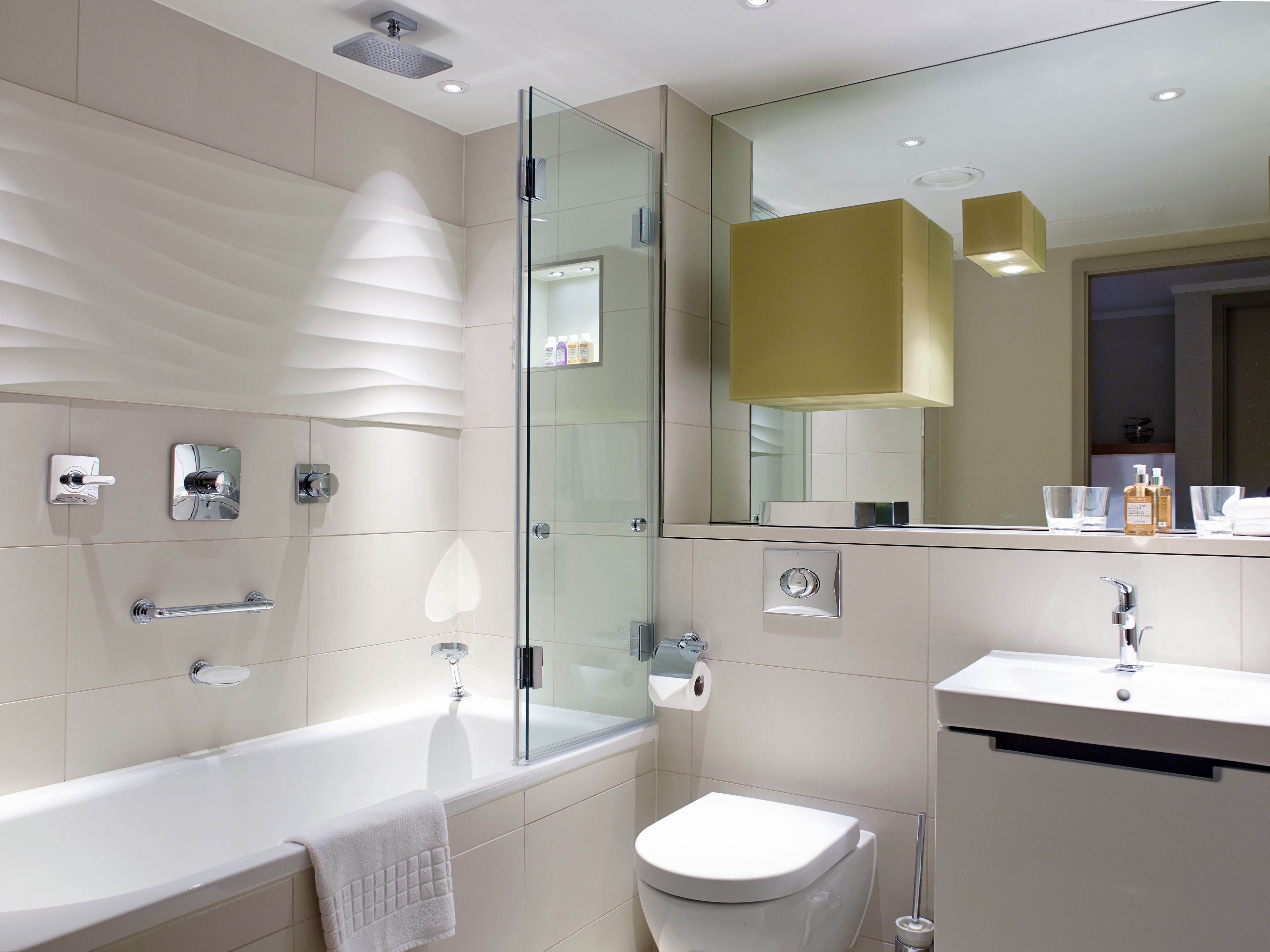A modern bathroom with a glass-enclosed shower, a white bathtub, a toilet, and a sink with a mirror above.