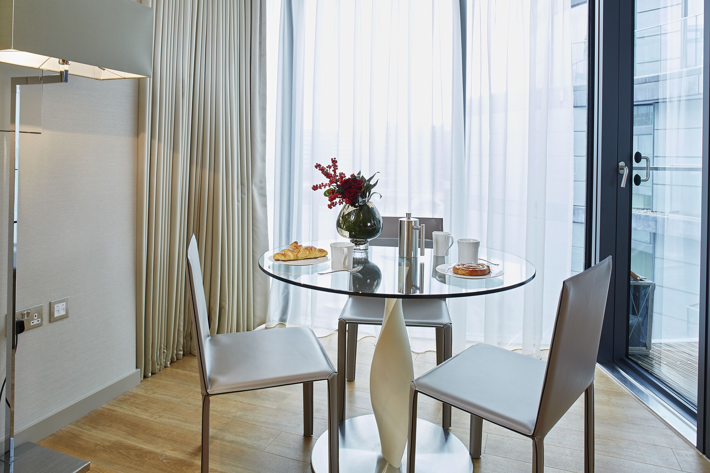 Een moderne eetruimte met een ronde glazen tafel, witte stoelen en een vaas met bloemen.