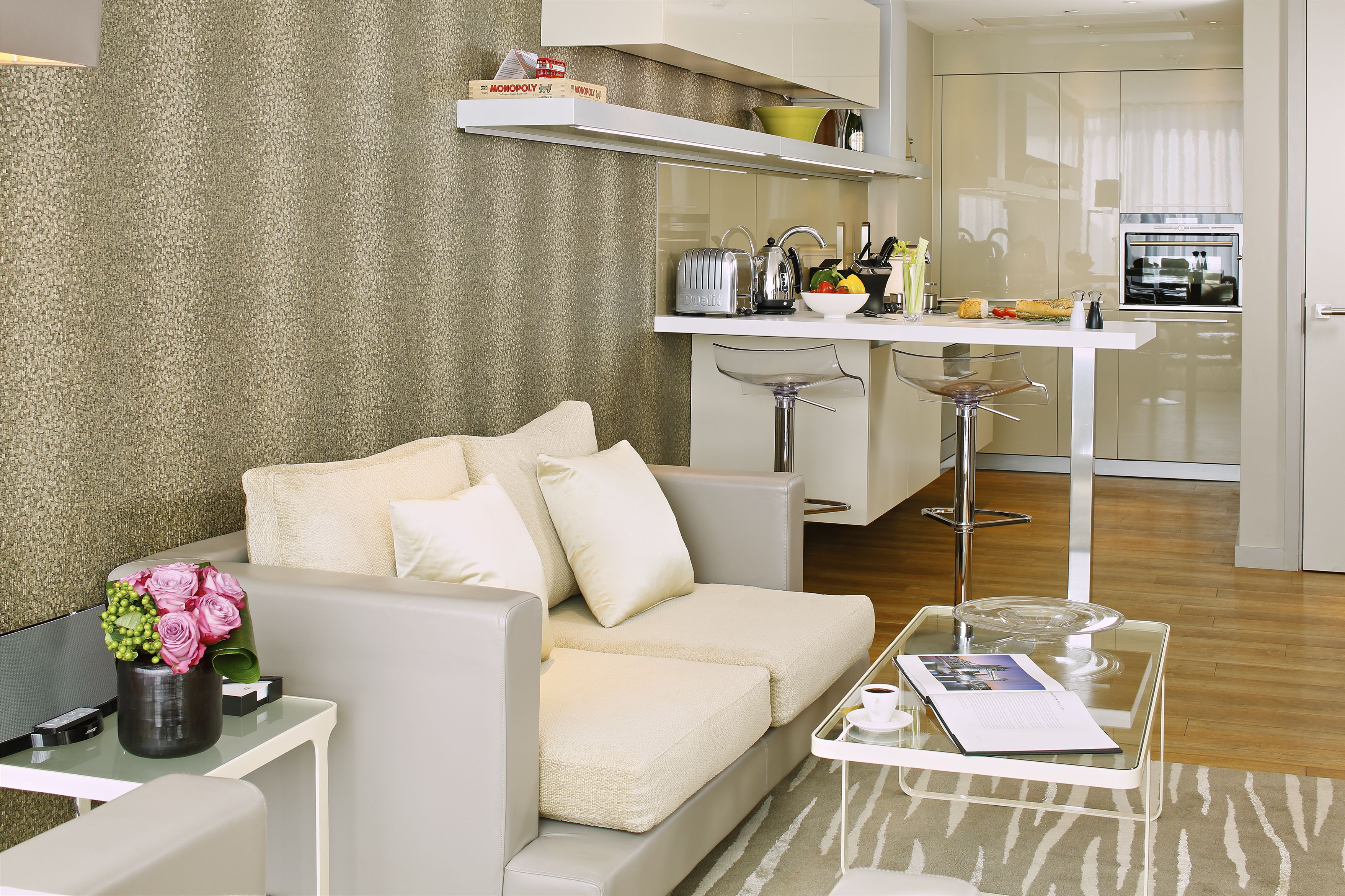 A modern living room with a sofa, a glass coffee table, and a small side table with a vase of flowers.