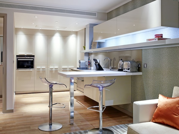 Una cocina moderna con una isla central, electrodomésticos de acero inoxidable y una zona de estar con dos taburetes de bar.