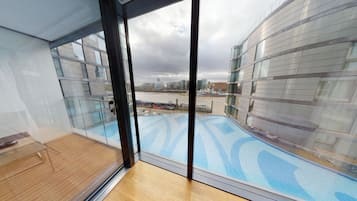 A modern hotel room with a large window overlooking a swimming pool and a cityscape.