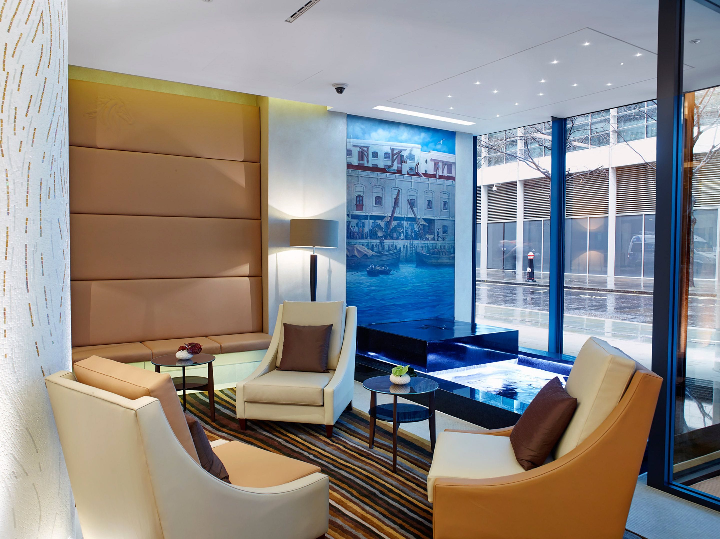 A modern hotel lobby with leather seating, a large window, and a mural of a cityscape.