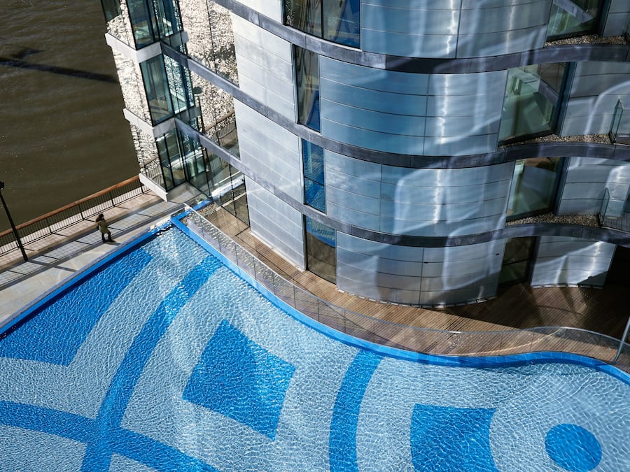 A modern building with a glass facade and a pool with blue mosaic tiles.