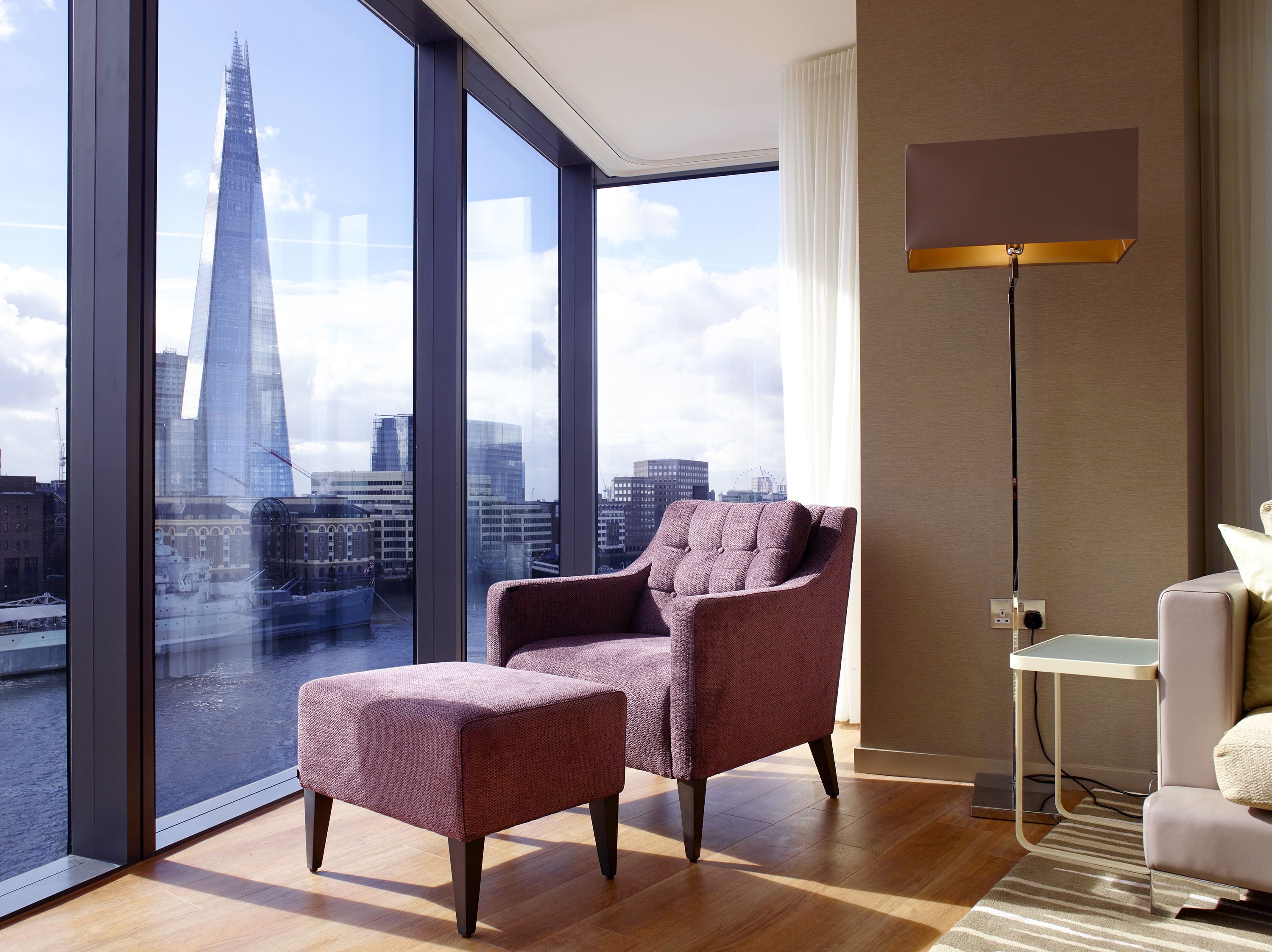 Una camera d'albergo moderna con un'ampia finestra che offre vista su uno skyline urbano, inclusa un'imponente torre.