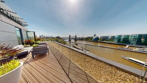 A rooftop terrace with seating, a view of the river, and modern buildings in the background. - Cheval Three Quays at The Tower of London (London)