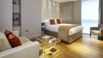 Ein modernes Hotelzimmer mit Bett, Sofa, Glastisch und Blick auf die Stadt.