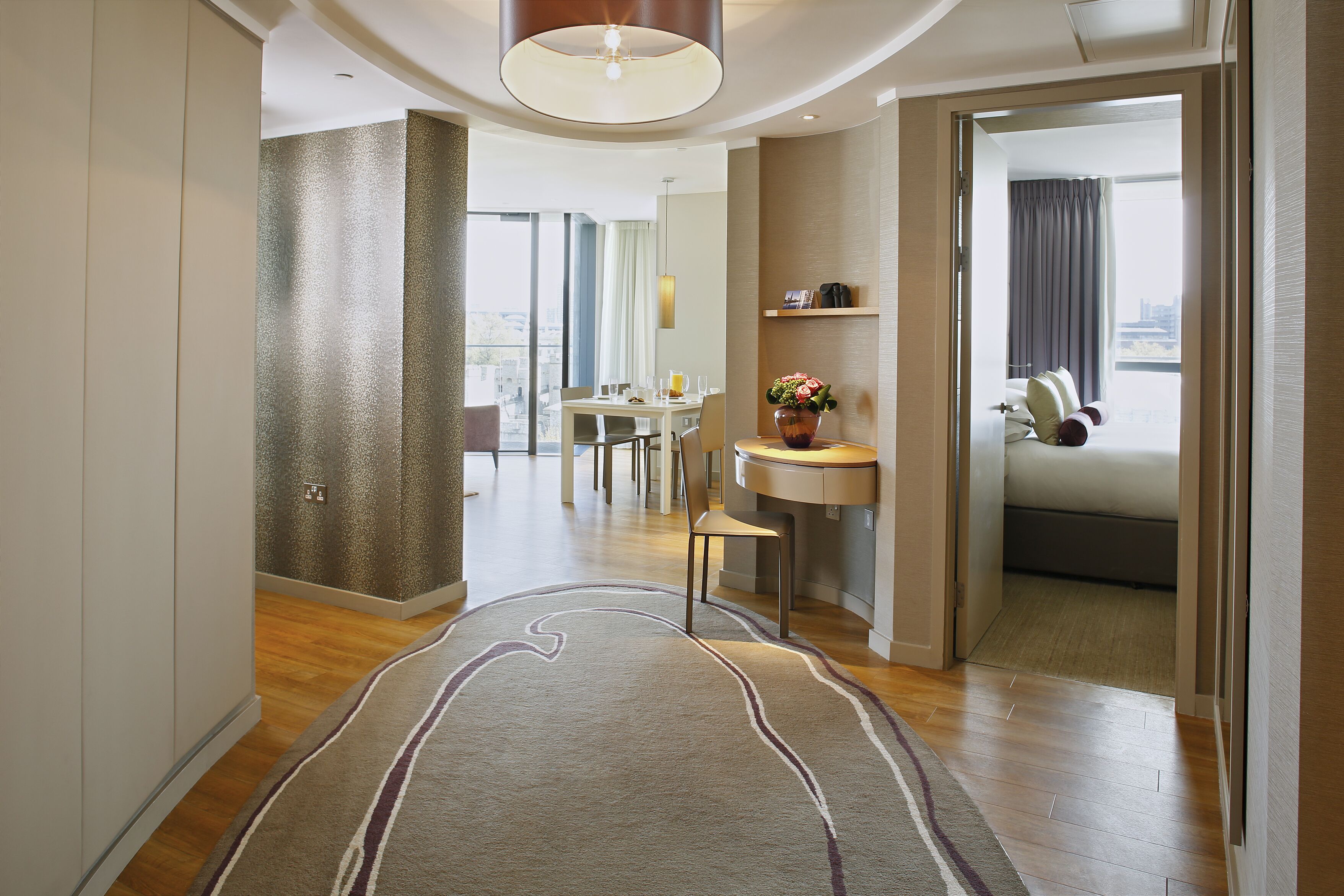 A modern hotel room with a dining area, a small kitchen, and a view of the city.