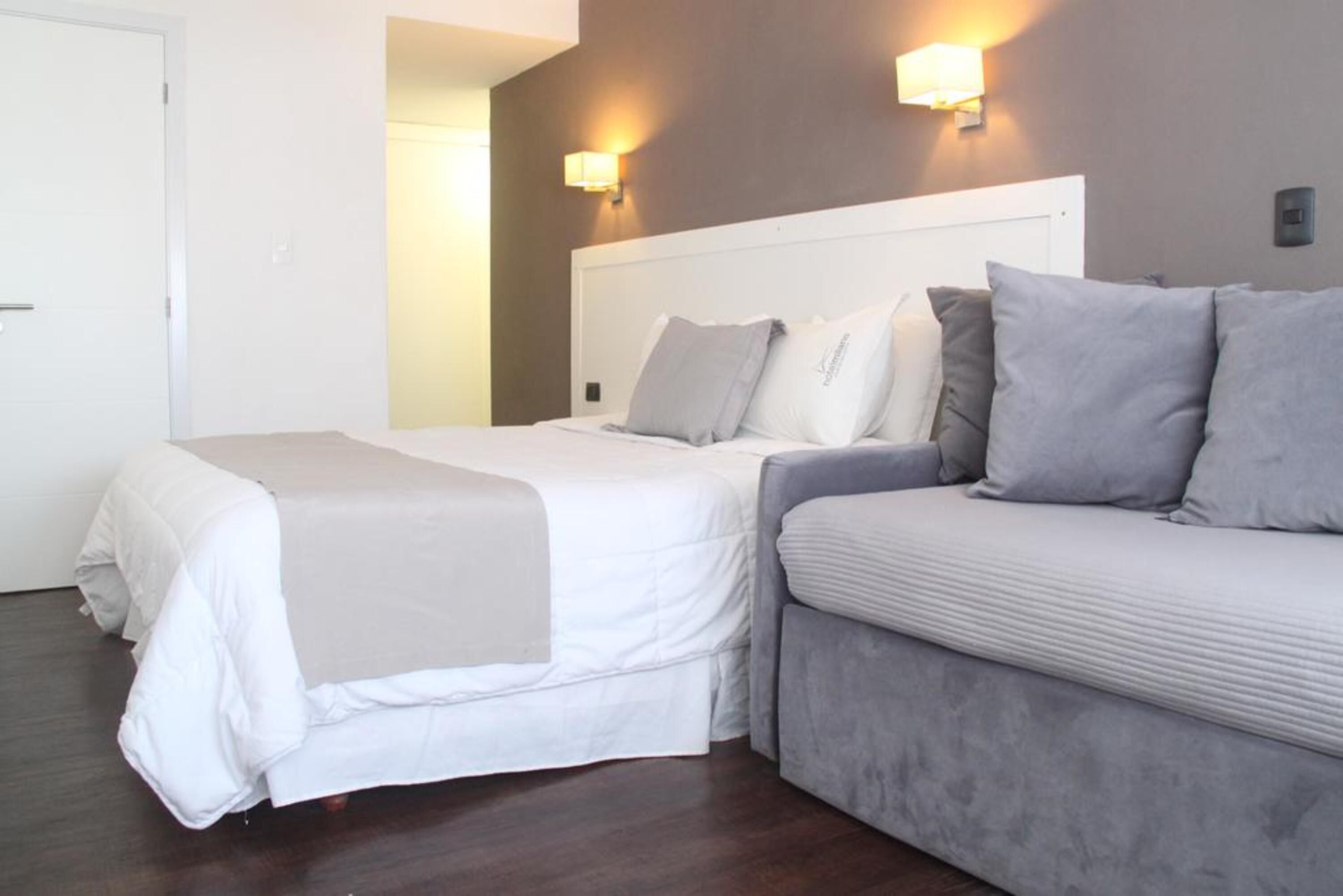 Habitación de hotel con cama, sofá y dos luces fijadas a la pared.