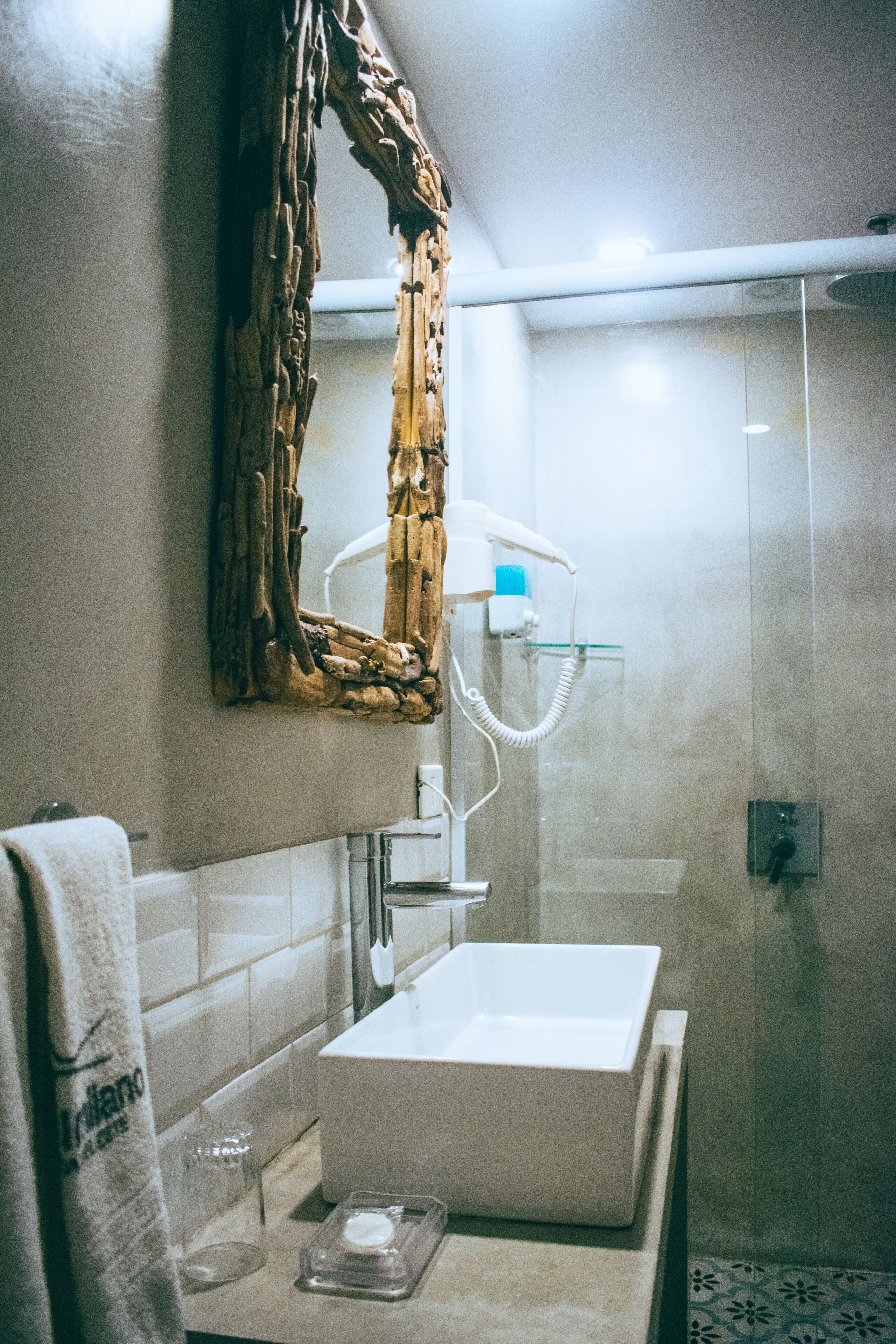 Un baño con un lavamanos blanco, cabina de ducha con mampara de vidrio y un espejo decorativo.