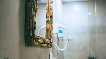 Un baño con un lavamanos blanco, cabina de ducha con mampara de vidrio y un espejo decorativo.