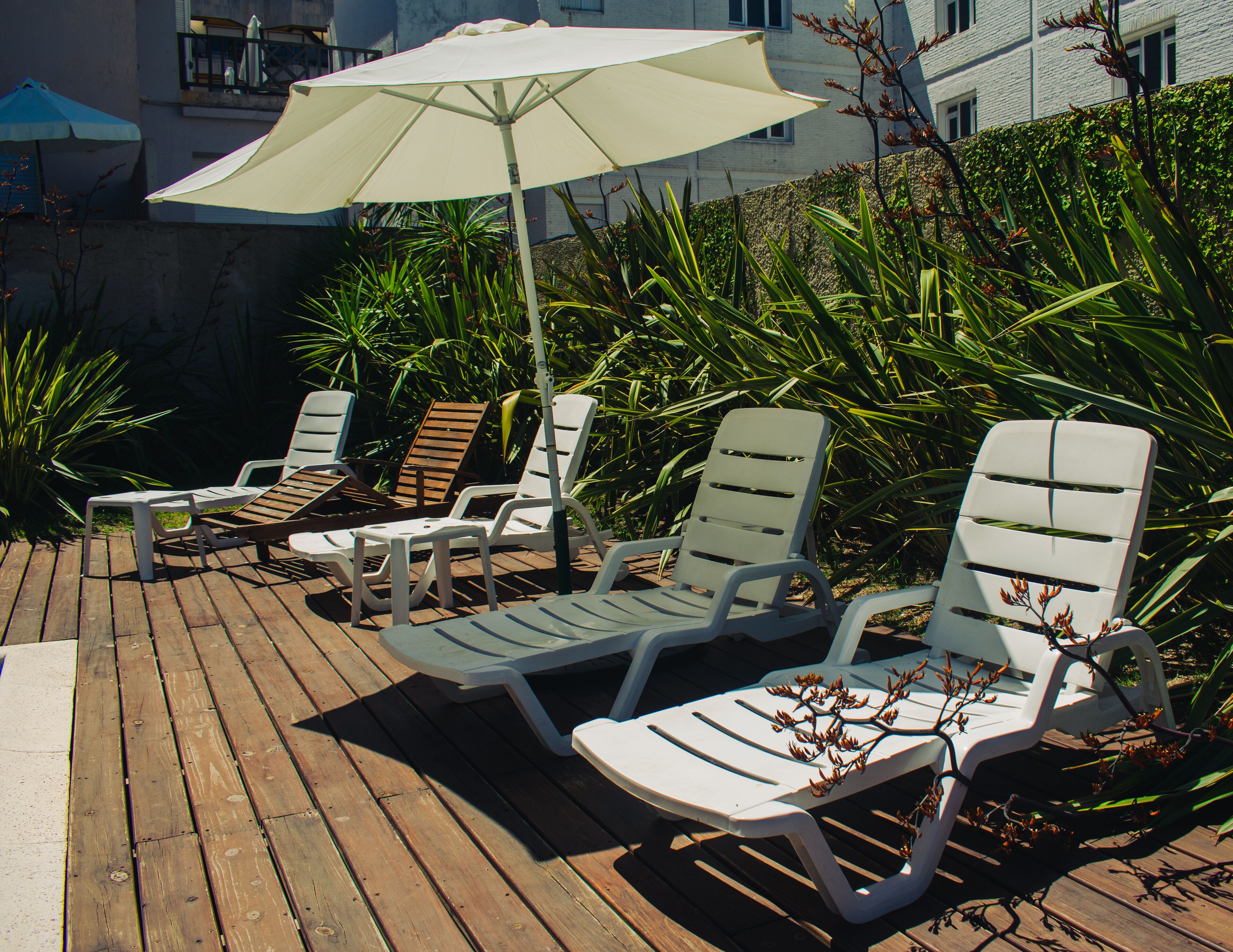 Een houten terras met witte ligstoelen en een grote parasol die schaduw biedt.