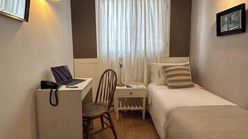 Una habitación pequeña y ordenada, con escritorio, silla y dos camas.