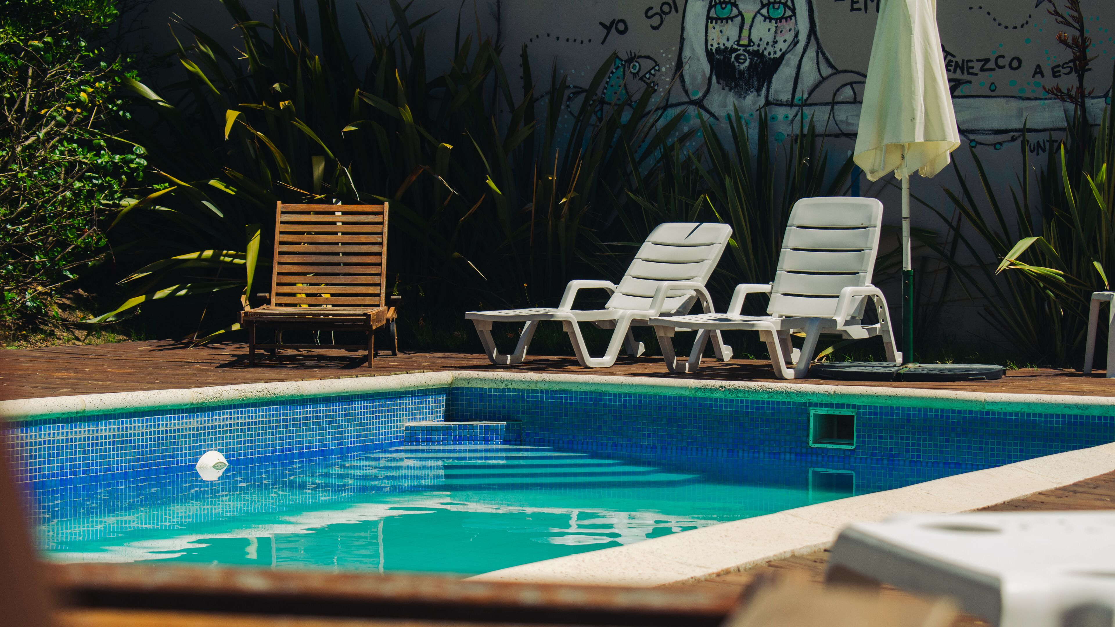 A swimming pool with two white lounge chairs and a wooden chair.