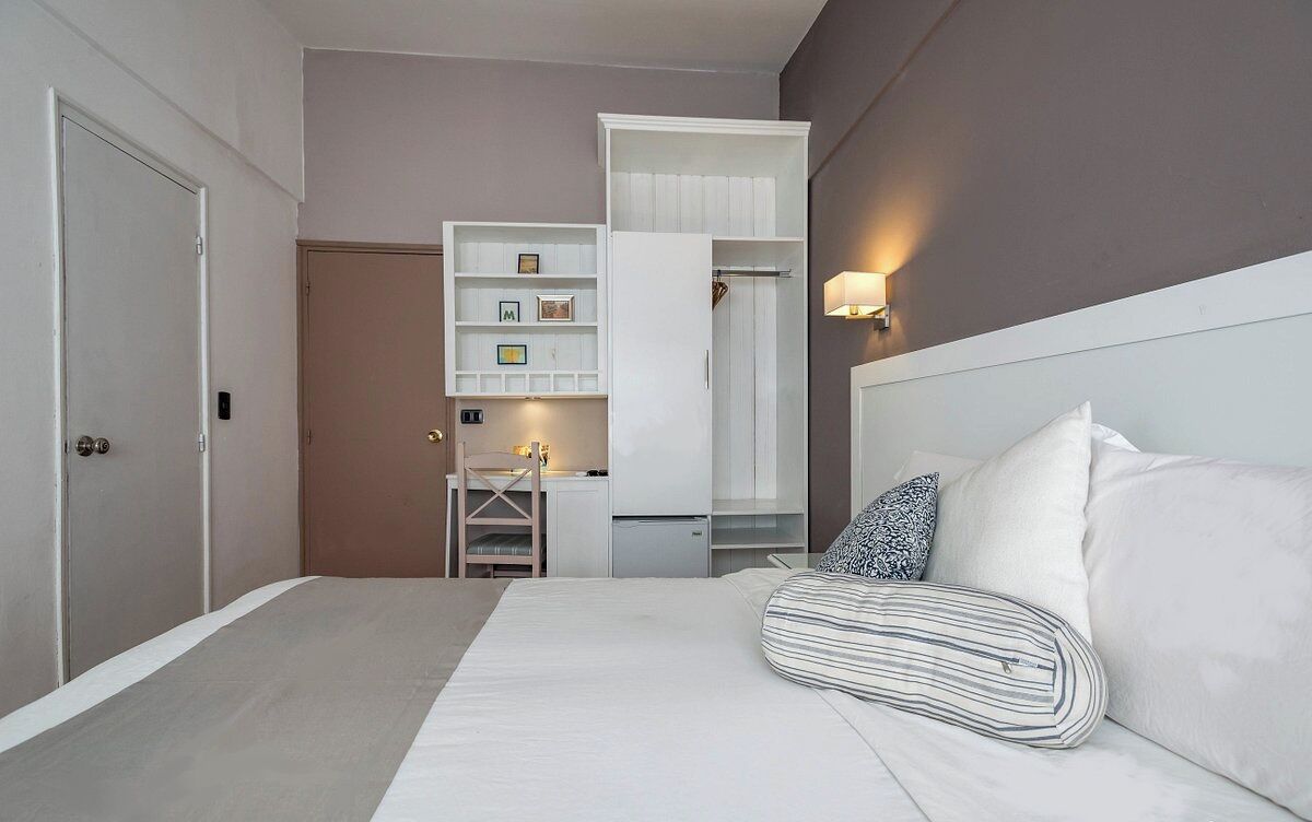 Una habitación de hotel con cama, escritorio, armario y espejo.