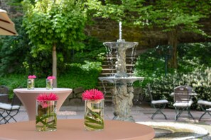 A garden setting with a fountain, two tables with vases of flowers, and outdoor seating. - Parkhotel Engelsburg (Recklinghausen)