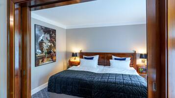 A hotel room with a large bed, two bedside lamps, a nightstand, a painting on the wall, and a wooden door frame.