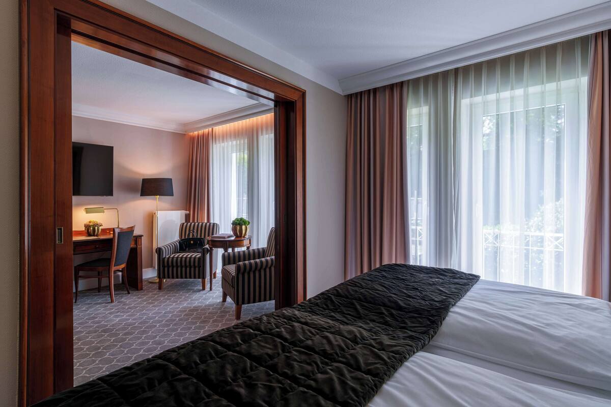 A hotel room with a large bed, a desk with a chair, a small table with a plant, and a TV on the wall.