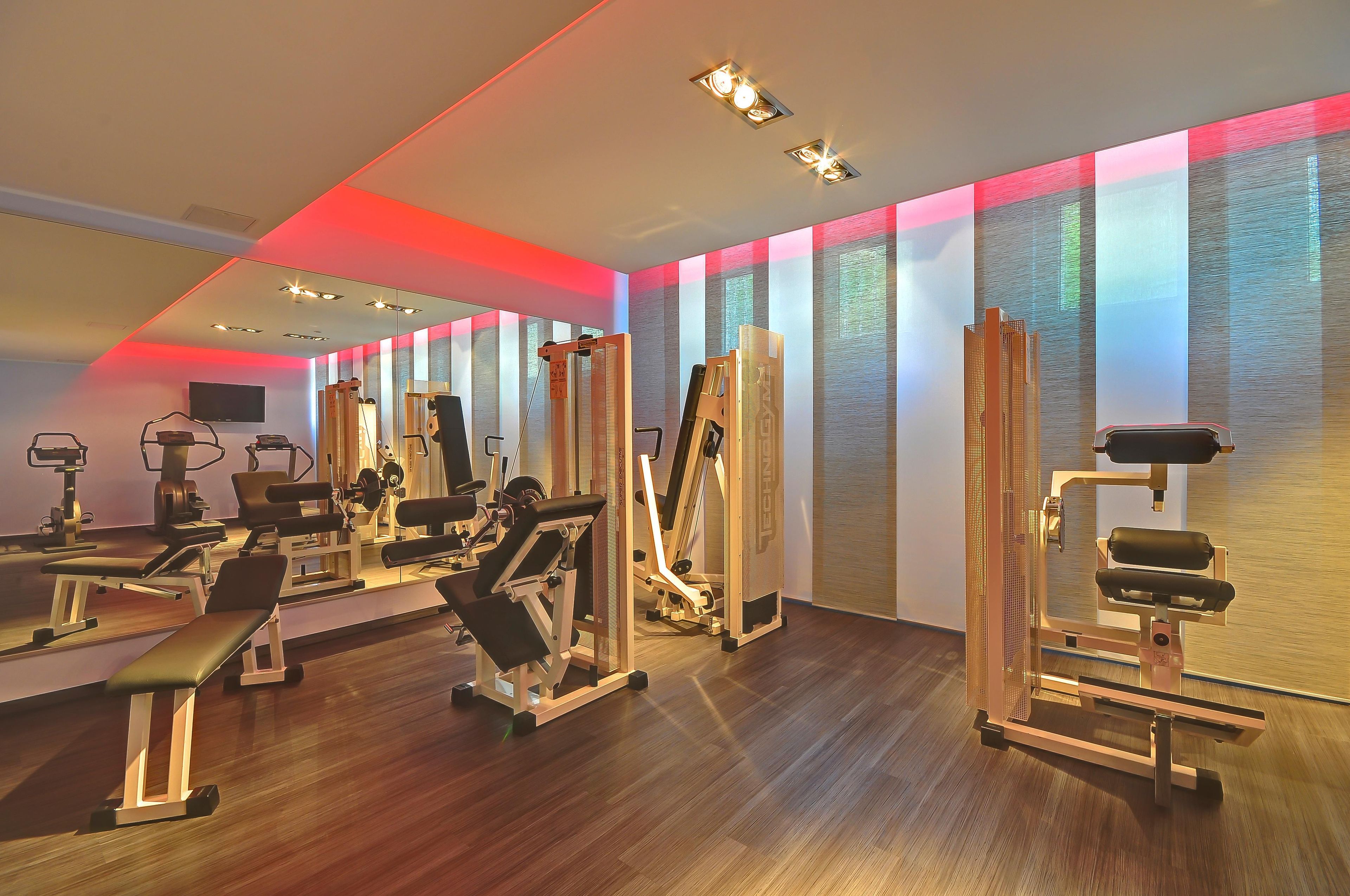 Ein Fitnessstudio mit unterschiedlichen Trainingsgeräten, einem großen Spiegel und einer Wand mit strukturierter Oberfläche.