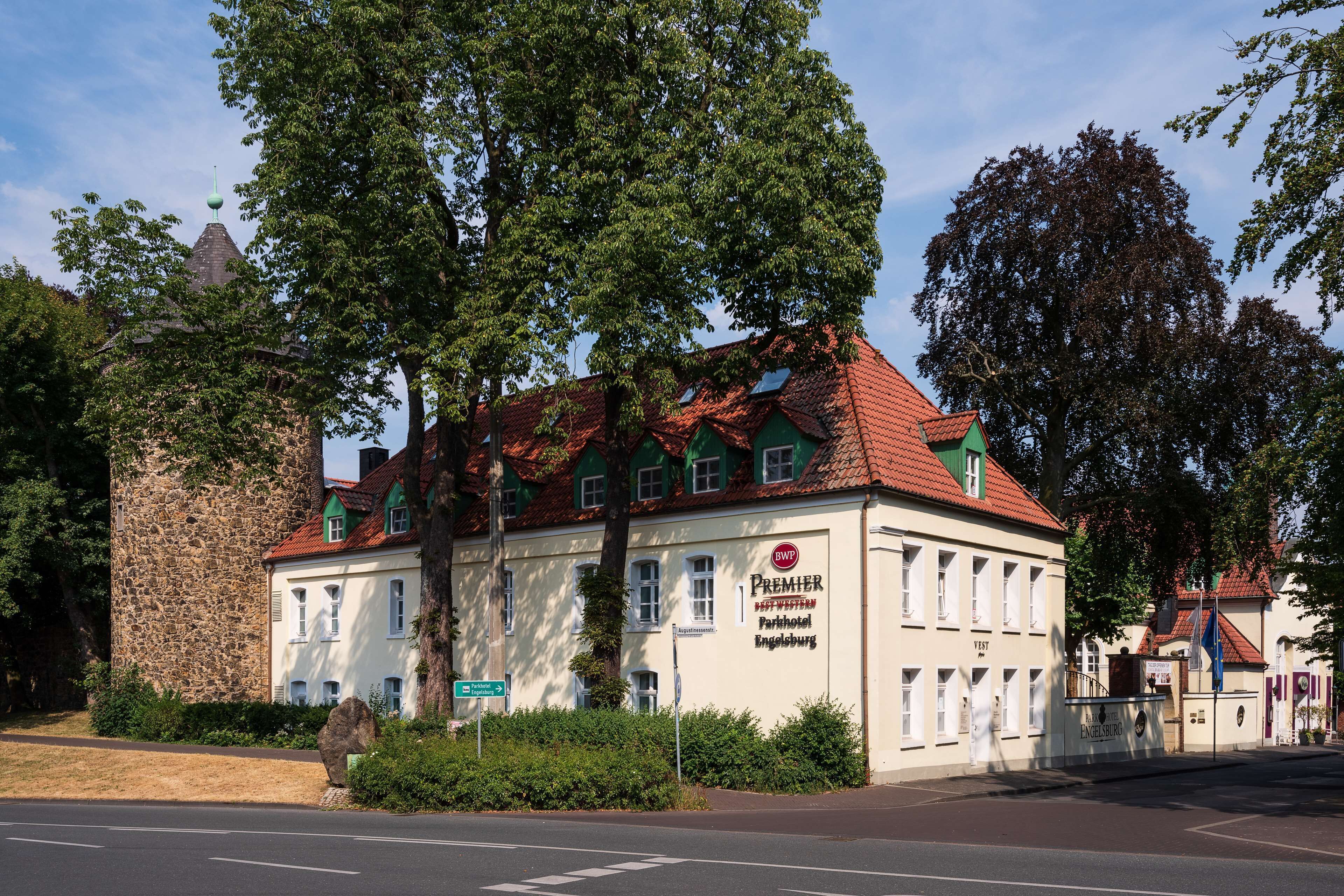 A hotel with a red-tiled roof, a stone wall, and a sign indicating it is a Premier Parkhotel in Engelsburg.