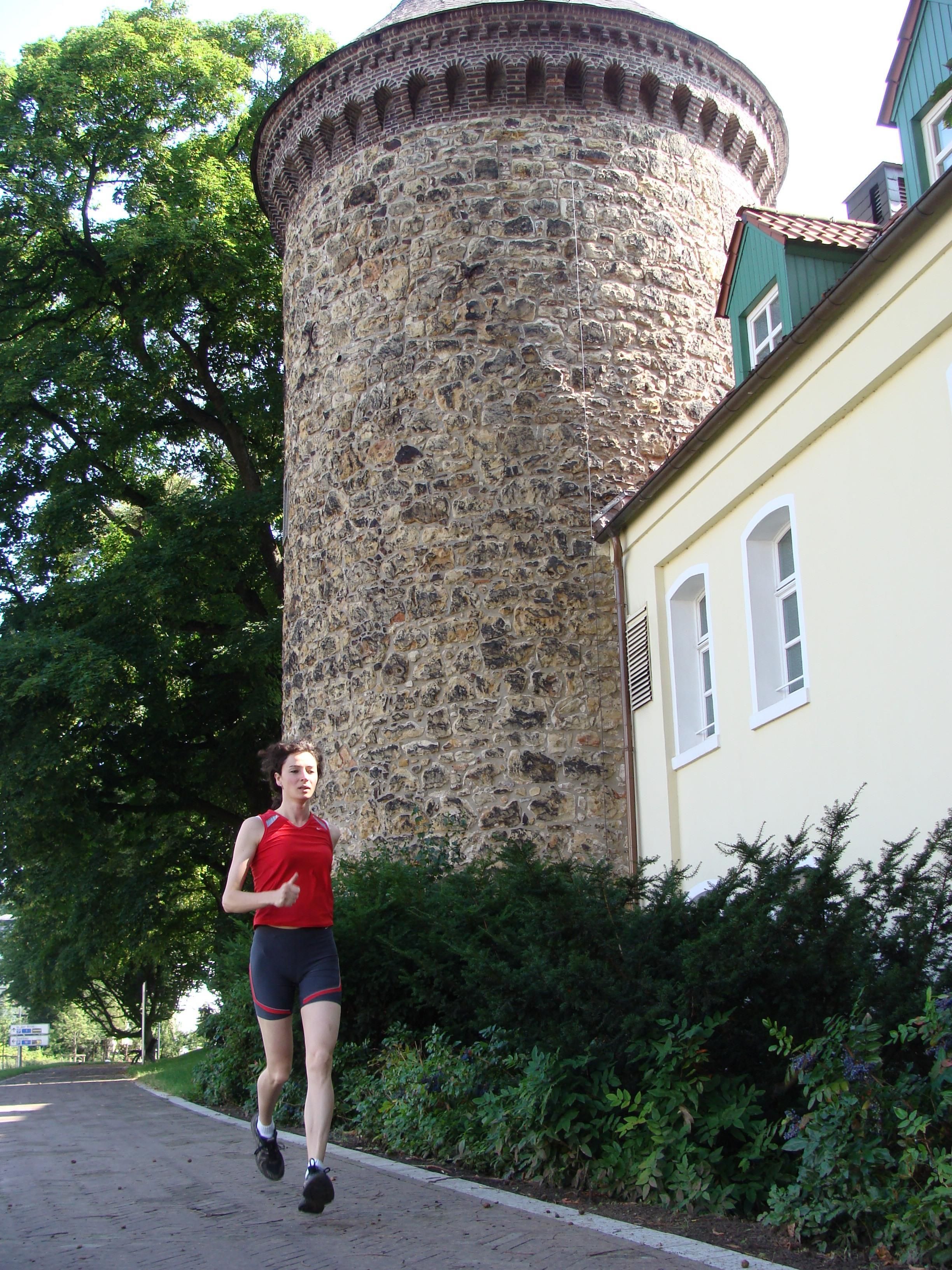 Une personne fait du jogging devant une tour de pierre historique, à côté de laquelle se trouve un bâtiment.