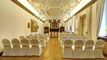 A formal room with rows of chairs, a piano, and ornate ceiling details.