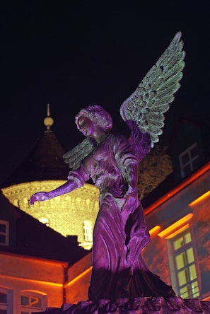 A statue of an angel with wings, positioned outdoors at night with a building in the background. - Parkhotel Engelsburg (Recklinghausen)