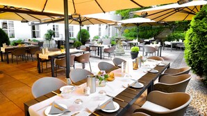Un área de comedor al aire libre con mesas preparadas para el servicio, sombrillas que dan sombra y una fuente como centro de atención.