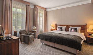 A hotel room with a large bed, a chair, a small table with a lamp, and a view of the outdoors through sheer curtains. - Parkhotel Engelsburg (Recklinghausen)