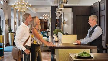 A hotel reception area with a wooden reception desk, a plant on the counter, and a plate of green peas on a table.