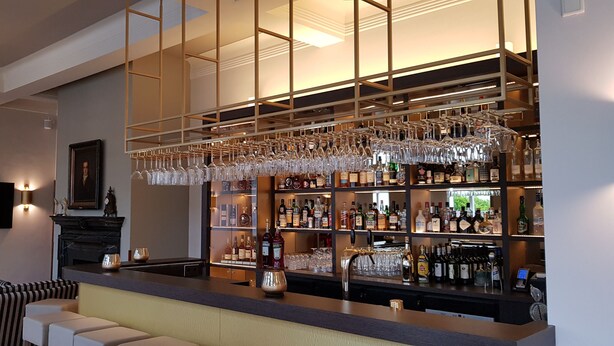 Zona de bar con diseño moderno, que incluye una barra con una variedad de licores y vasos.