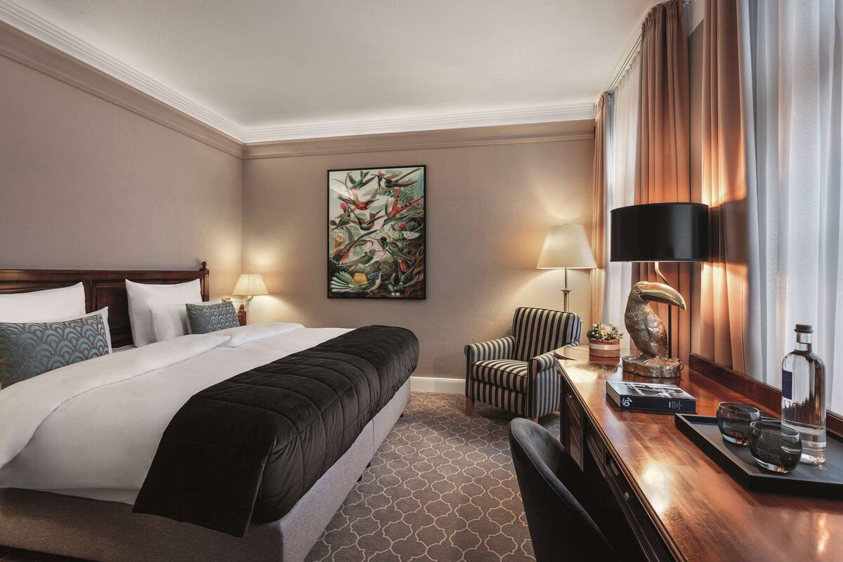 A hotel room with a large bed, a desk with a lamp, a chair, and a decorative sculpture.