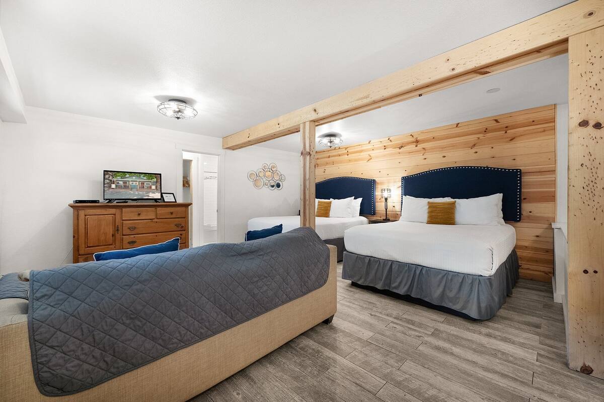 A bedroom with two beds, wooden ceiling beams, a dresser, and a wall-mounted TV.