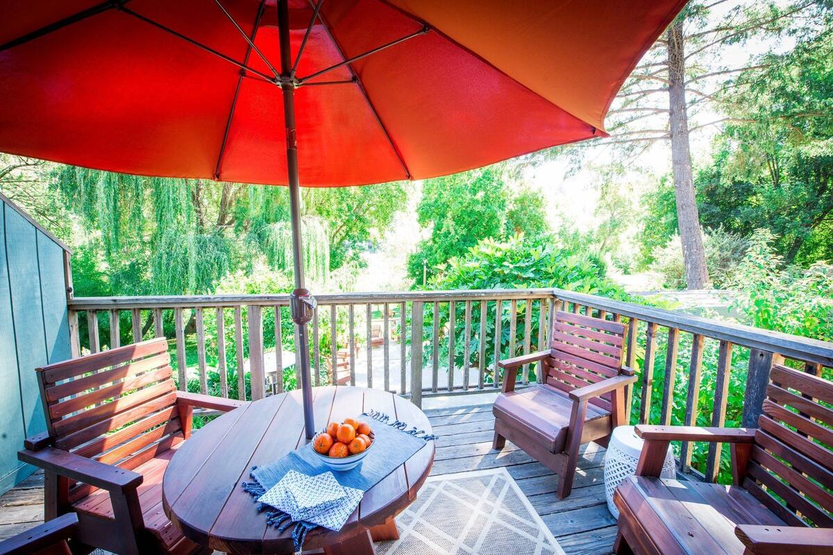 A wooden deck with a round table, chairs, and a red umbrella.