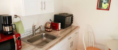 A kitchen with white cabinets, a stainless steel sink, a red microwave, a black toaster, and a wooden chair.