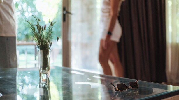 Une table en verre ornée d’un vase contenant des plantes vertes et d’une paire de lunettes de soleil.