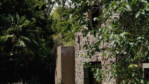 Un bâtiment en pierre doté d’une porte d’entrée, entouré d’une végétation luxuriante et accessible par un chemin de pierre.