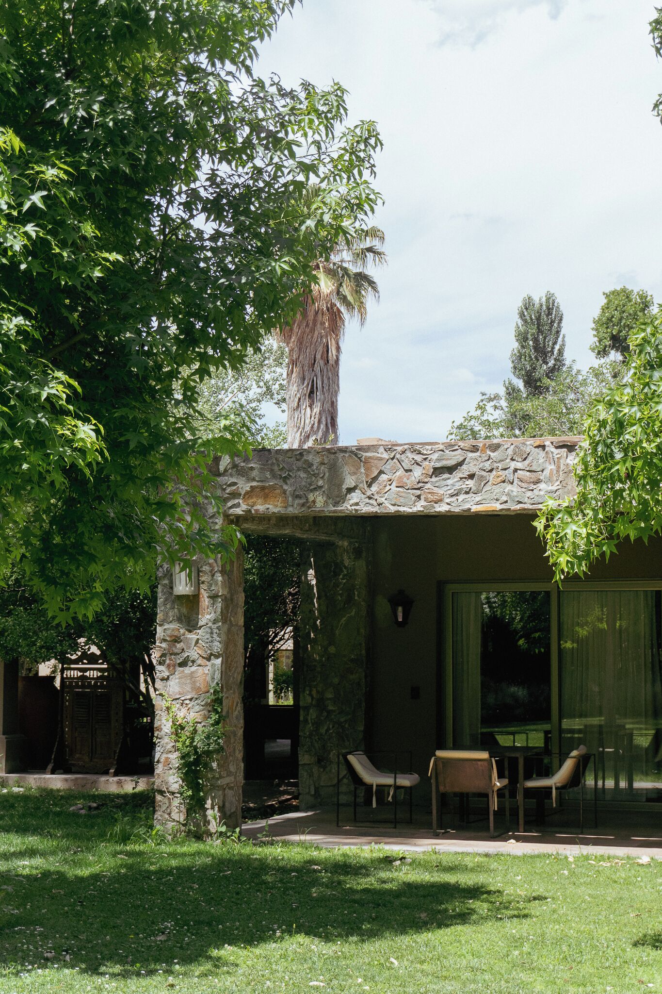 Un edificio de piedra con un patio cubierto, mesas al aire libre y un árbol grande en primer plano.