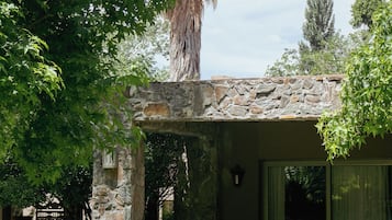 Un edificio de piedra con un patio cubierto, mesas al aire libre y un árbol grande en primer plano.