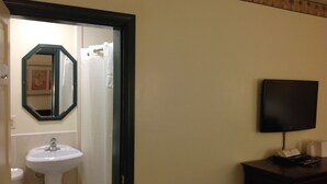A bathroom with a white sink, a mirror, and a television mounted on the wall. - Budget Inn (Salisbury)