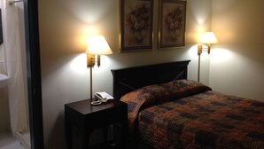 A hotel room with a bed, two bedside lamps, a telephone on a bedside table, and two framed floral paintings on the wall. - Budget Inn (Salisbury)