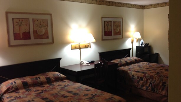 A hotel room with two beds, a desk with a telephone, two lamps, and framed artwork on the walls. - Budget Inn (Salisbury)