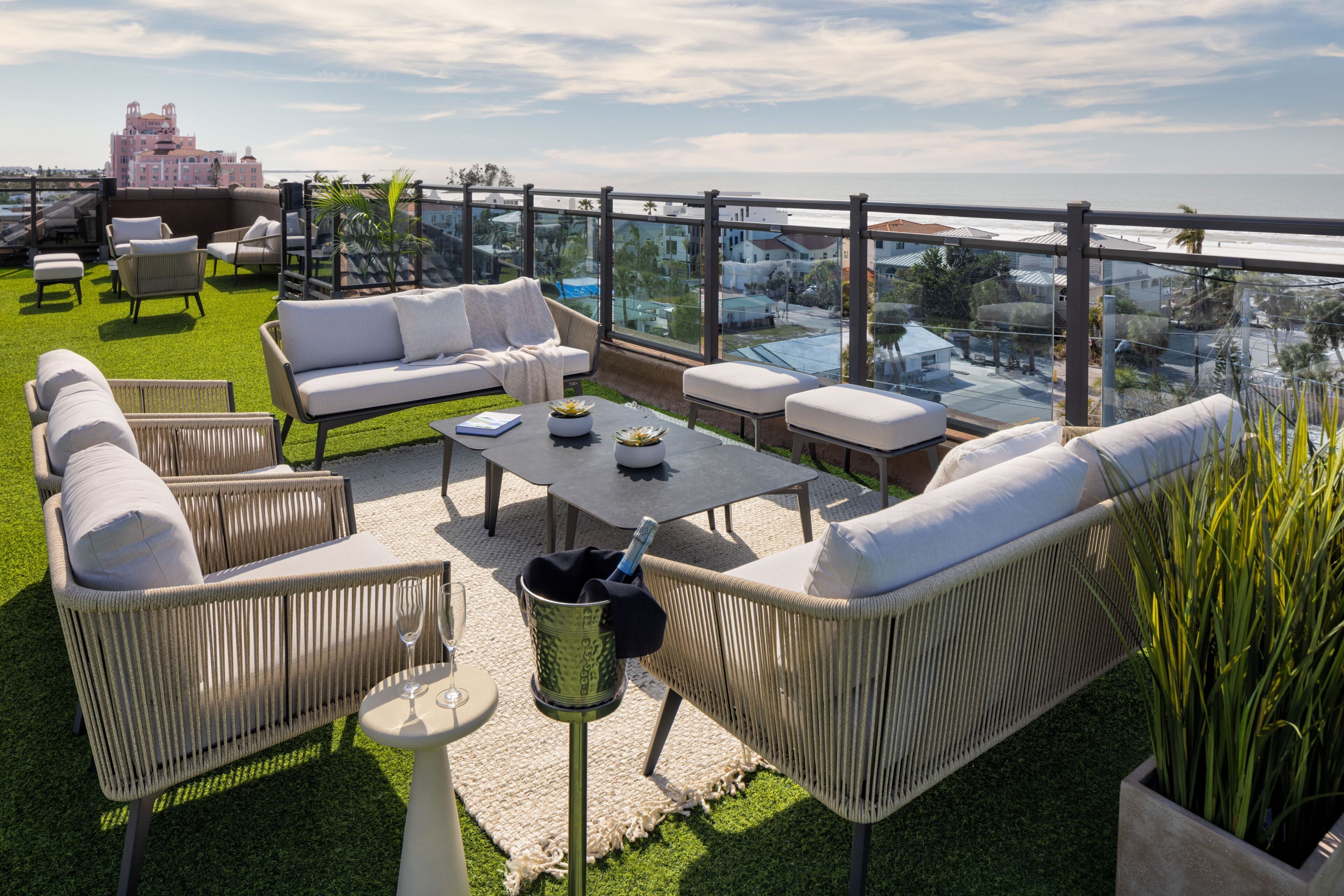 A rooftop terrace with wicker furniture, a table, and a view of the city and ocean.