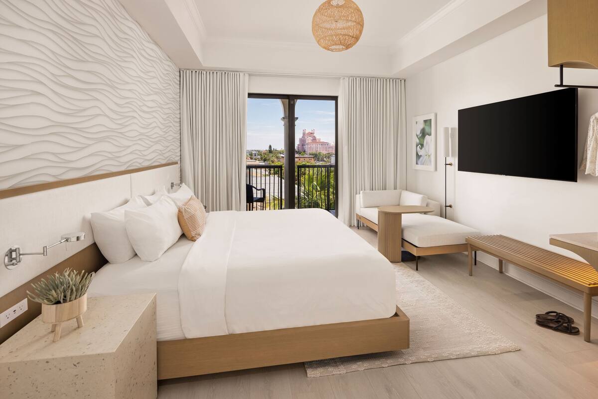 Une chambre d’hôtel moderne dotée d’un grand lit, d’une télévision à écran plat, d’un balcon offrant une vue sur la ville et d’un petit coin salon.