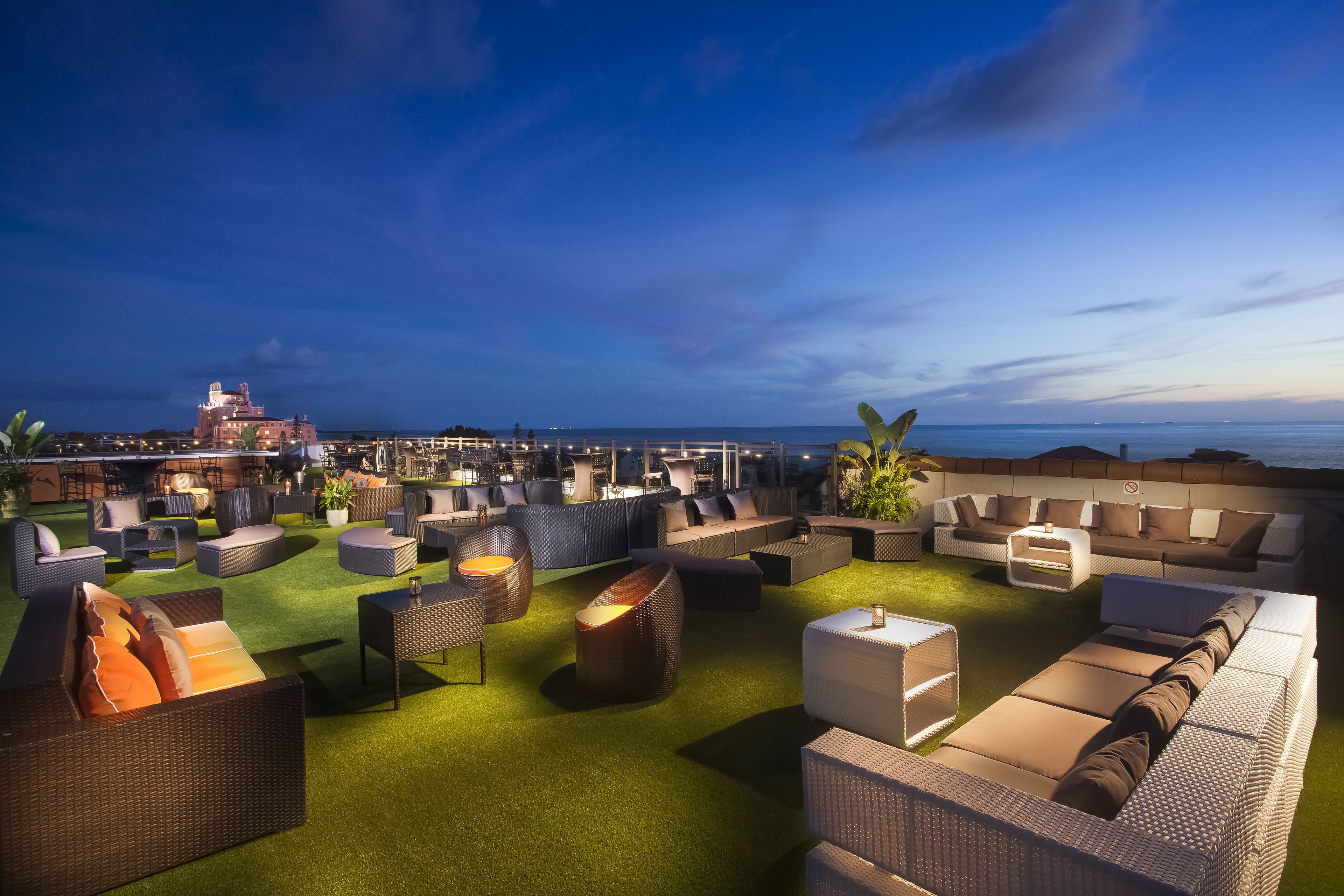 Un área de lounge en la azotea con diversas opciones de asientos, incluyendo sofás y sillones, sobre una alfombra verde.