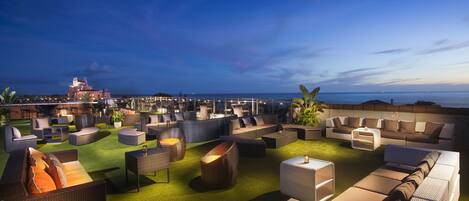 Un área de lounge en la azotea con diversas opciones de asientos, incluyendo sofás y sillones, sobre una alfombra verde.