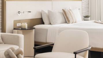 Una habitación de hotel moderna con una cama grande, una mesita de noche con lámpara, una silla y una pequeña planta en maceta.